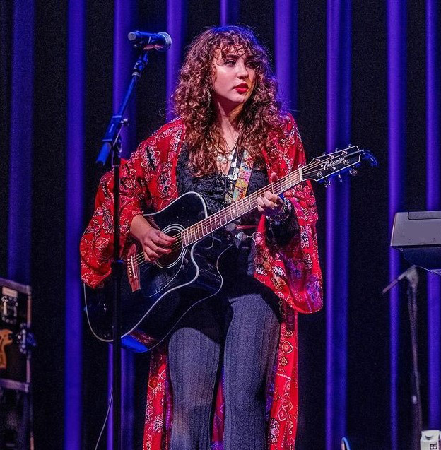 Calista Garcia holding a Takamine Guitar while performing on stage 